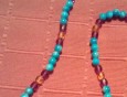 Ogrlica narejena z pretežno perlami turkizne barve.  Vmes nanizane perle rumene in temno vijolične barve