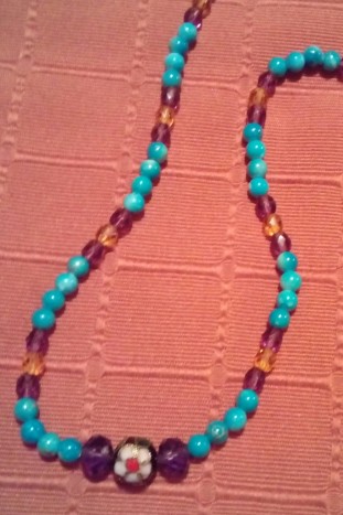 Turkizna ogrlica - Ogrlica narejena z pretežno perlami turkizne barve. Vmes nanizane perle rumene in temno vijolične barve